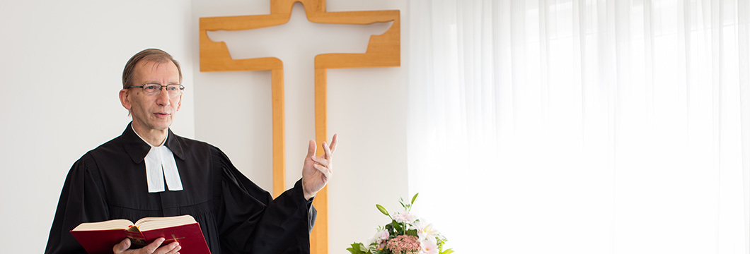 Der Pfarrer des Hauses steht vor dem Kreuz im Andachtsraum.