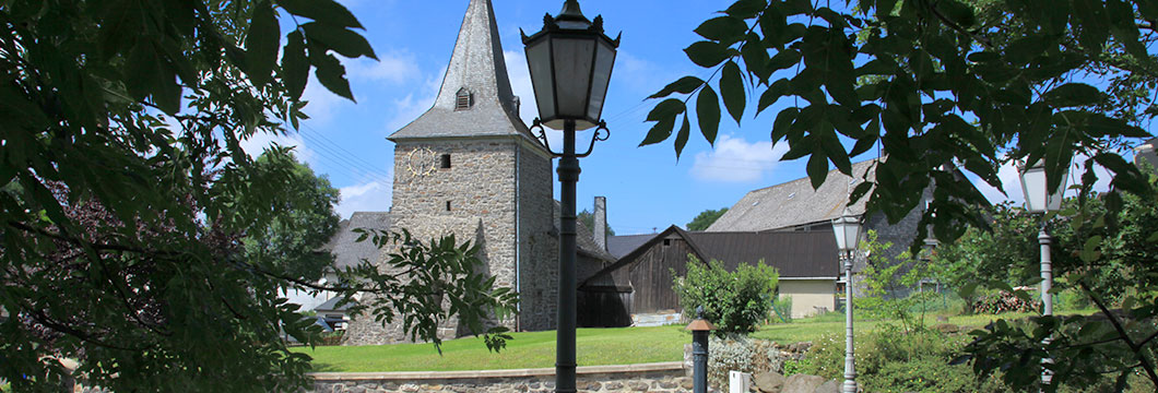Umgeben von Bäumen und Häusern liegt eine ältere Steinkirche.