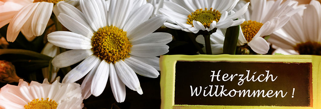 Inmitten von Blumen steht eine Tafel mit der Aufschrift: Herzlich willkommen!